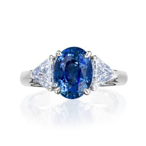 One three across ring in 18 karat white gold and platinum centrally set with an oval cut tanzanite shouldered by two trilliant cut diamonds